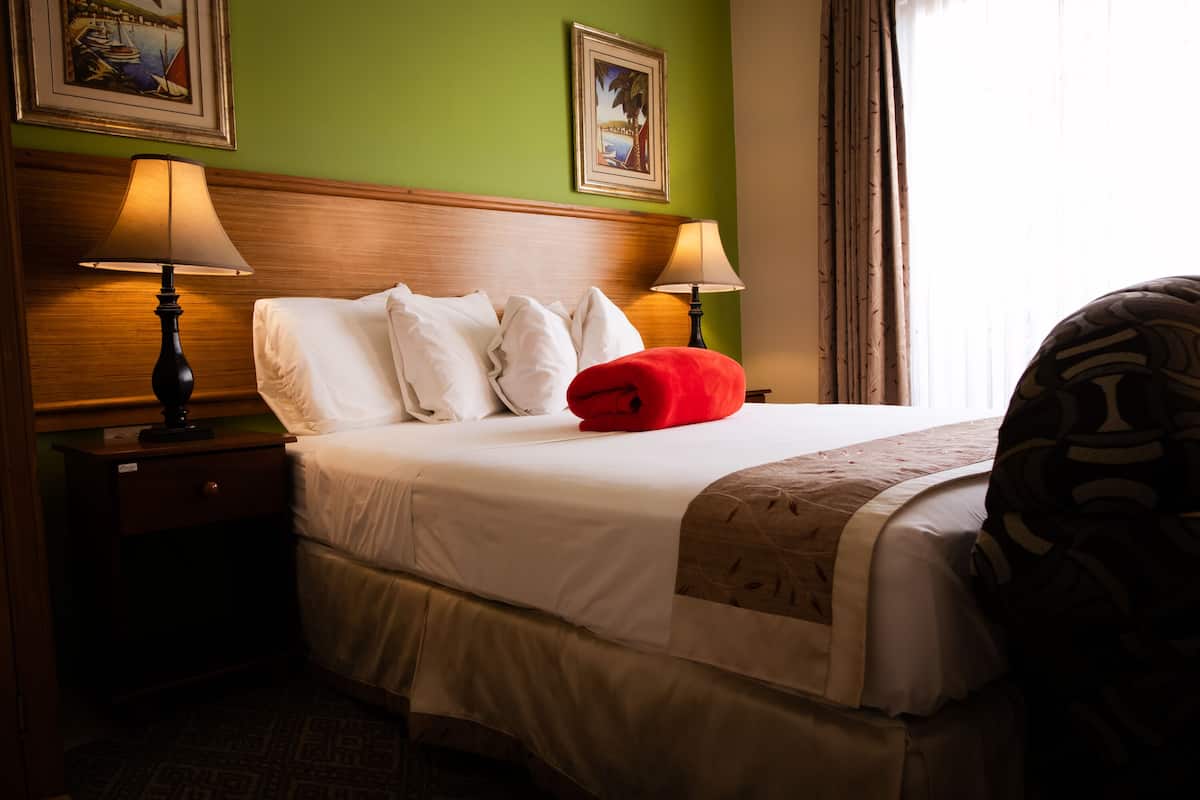 A hotel room with a large bed, two bedside lamps, a nightstand, and a window with curtains.