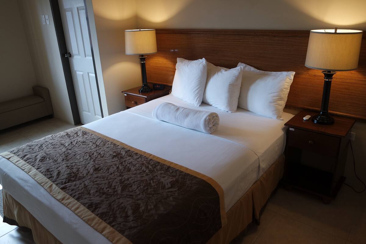 A neatly made bed with a brown patterned bedspread, two white pillows, and a rolled towel. There are two bedside lamps on wooden nightstands.