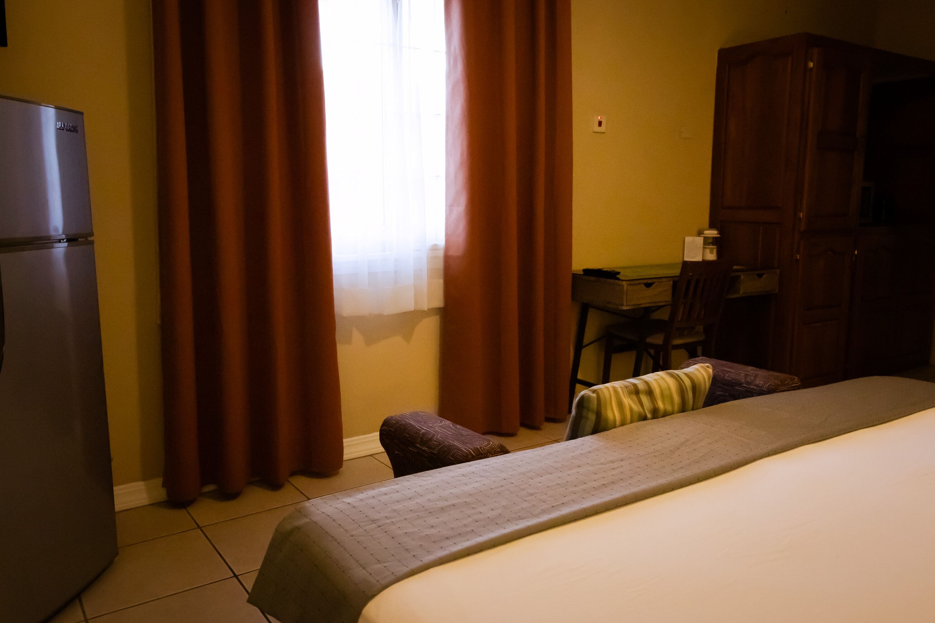 A hotel room with a bed, a desk, a chair, a wardrobe, and a refrigerator.