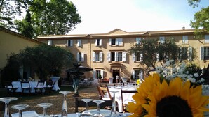 An outdoor dining area with tables set for a meal, a fountain, and a building in the background. - Château Rieutort (Saint-Pargoire)
