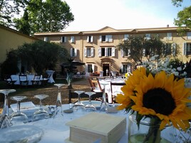 Un espacio de comedor al aire libre con mesas dispuestas para una comida, una fuente y un edificio al fondo.