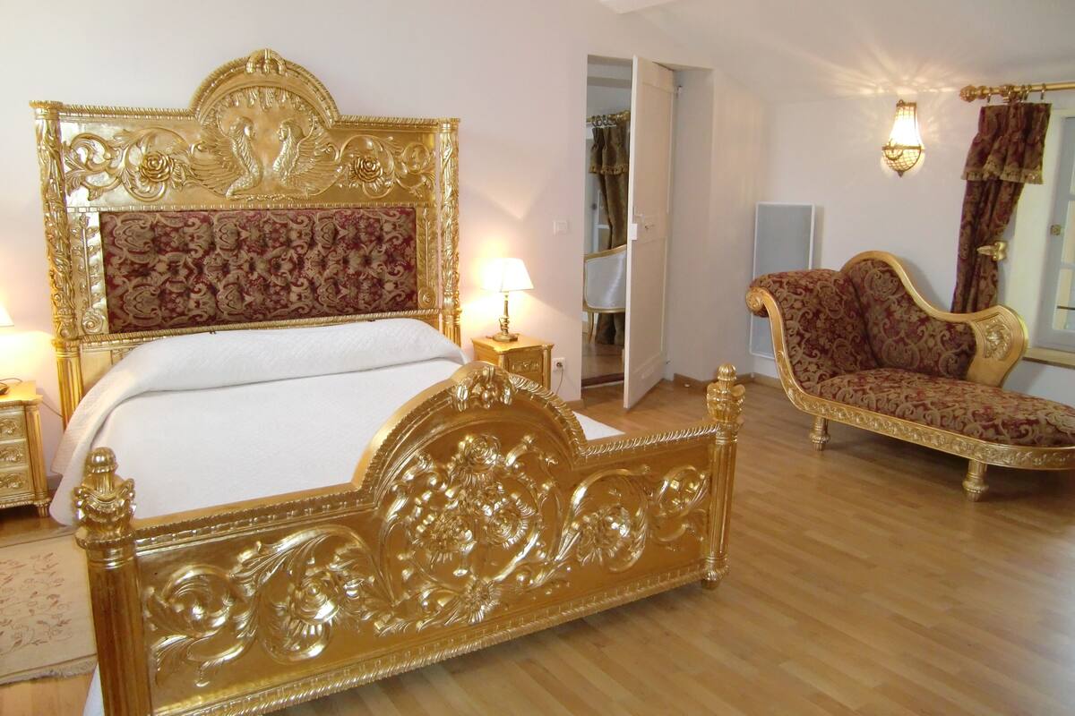 Una habitación con una cama grande y ornamentada, un sillón a juego y un espejo.