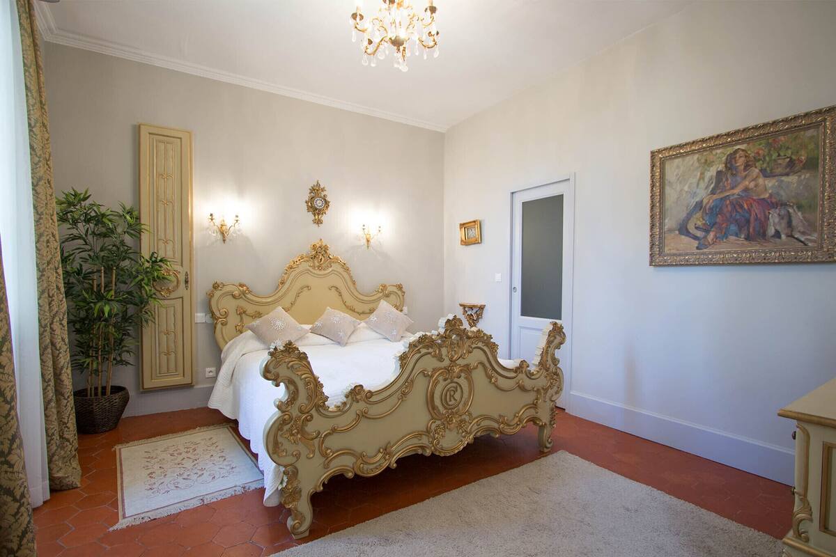 Un dormitorio con una cama grande y elaborada, una planta en maceta, un candelabro y un cuadro en la pared.