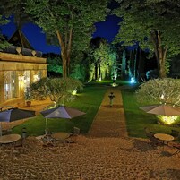 Un jardín nocturno con un camino pavimentado, mobiliario exterior y árboles iluminados.