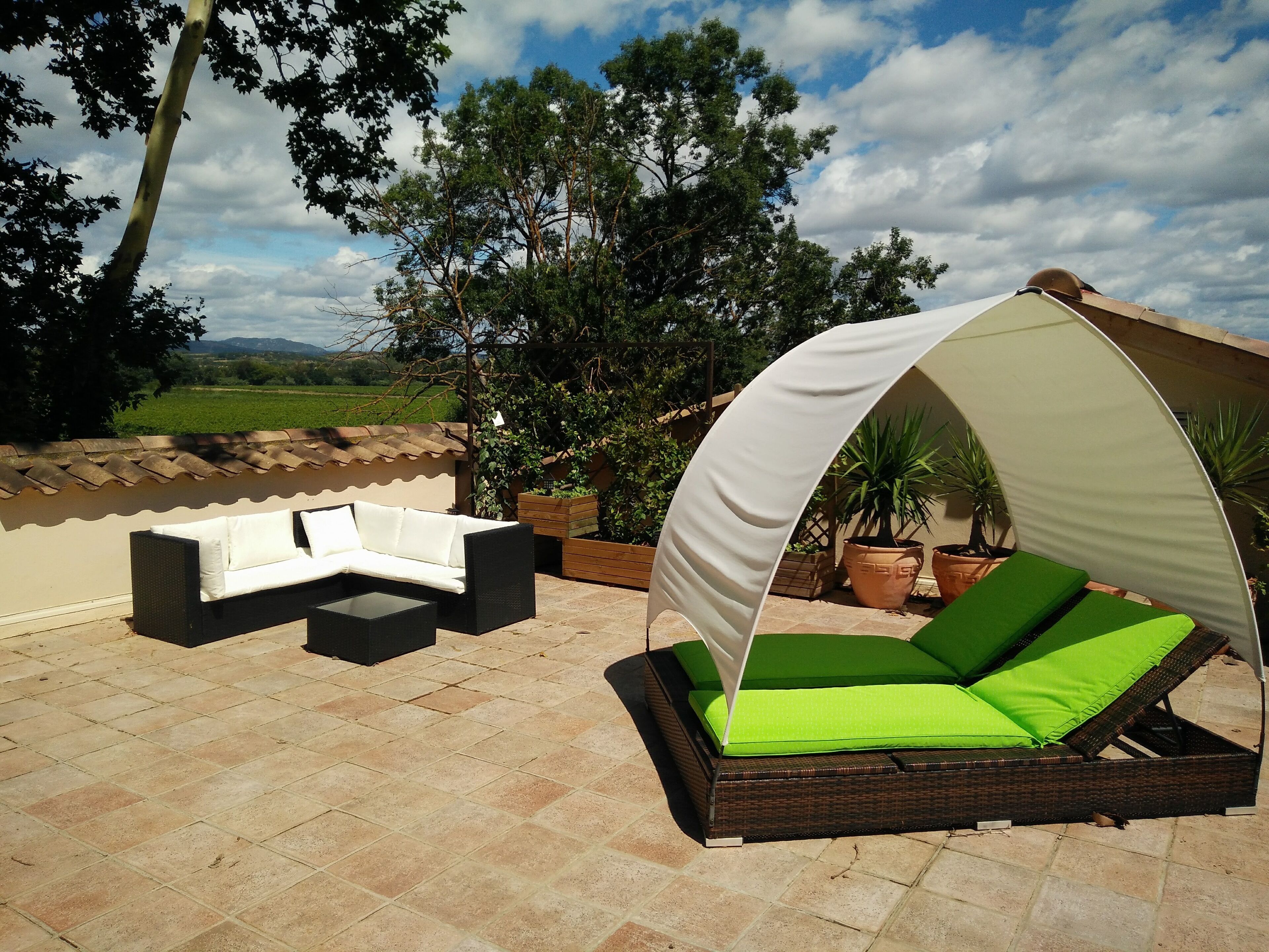 An outdoor patio with a white sofa, a green cushioned daybed, and potted plants.