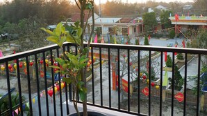 A balcony with a potted plant, a view of a street with colorful decorations, and a building in the background. - White Lion House (Da Nang)