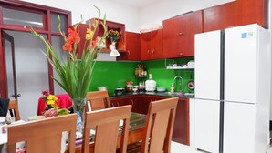 A kitchen with wooden cabinets, a white refrigerator, and a dining table with chairs. - White Lion House (Da Nang)