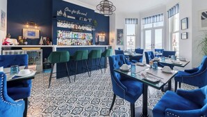 Eine Bar mit blauer Wand und einem gemusterten Boden, ausgestattet mit Barhocker und einer Theke mit verschiedenen Flaschen.