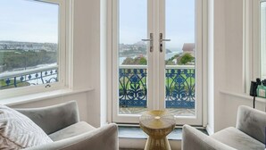 Ein Zimmer mit Blick auf eine Brücke und Grünflächen, ein Balkon mit blauer Geländer und zwei Sessel.