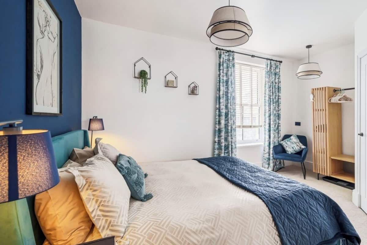 Un dormitorio con cama, lámparas de noche, armario y ventana con cortinas.