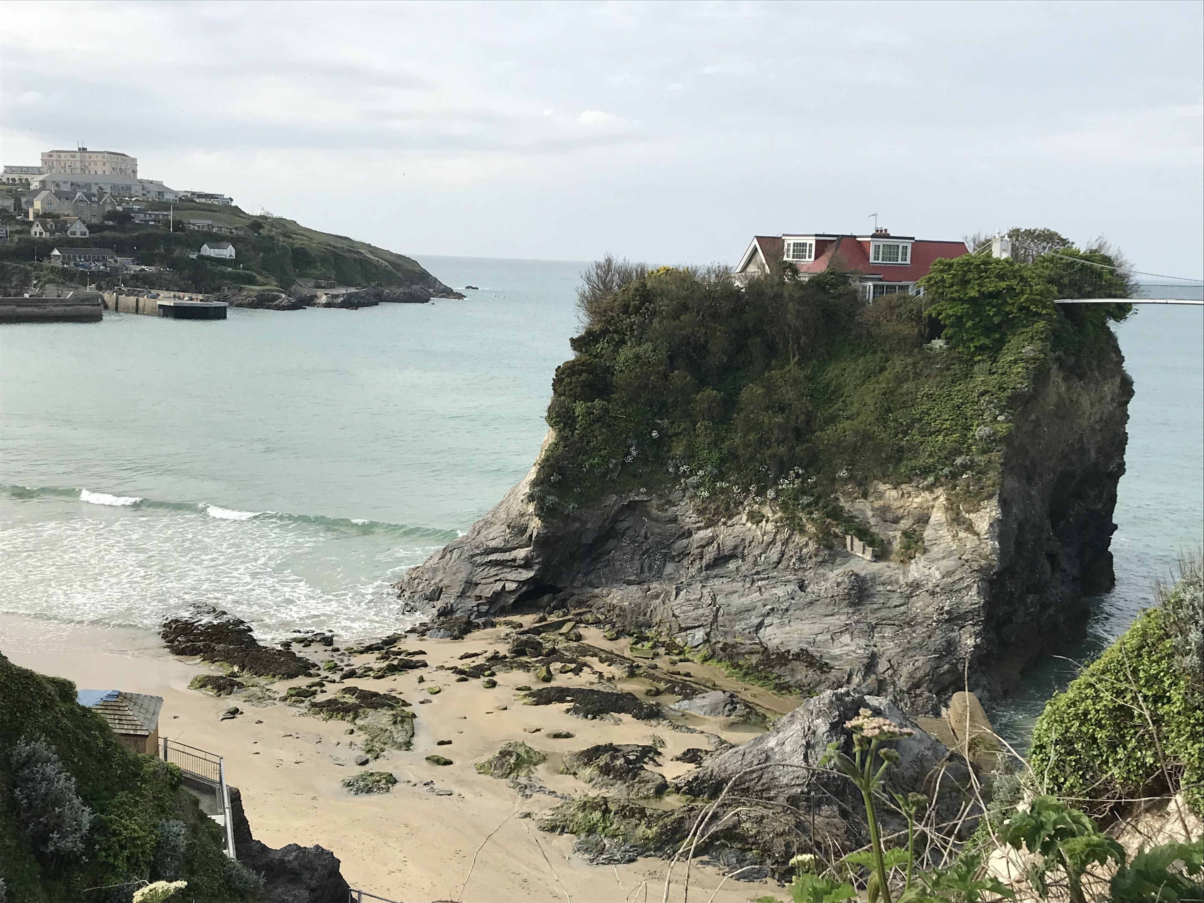 A coastal scene with a cliff, beach, and a building on a hill.