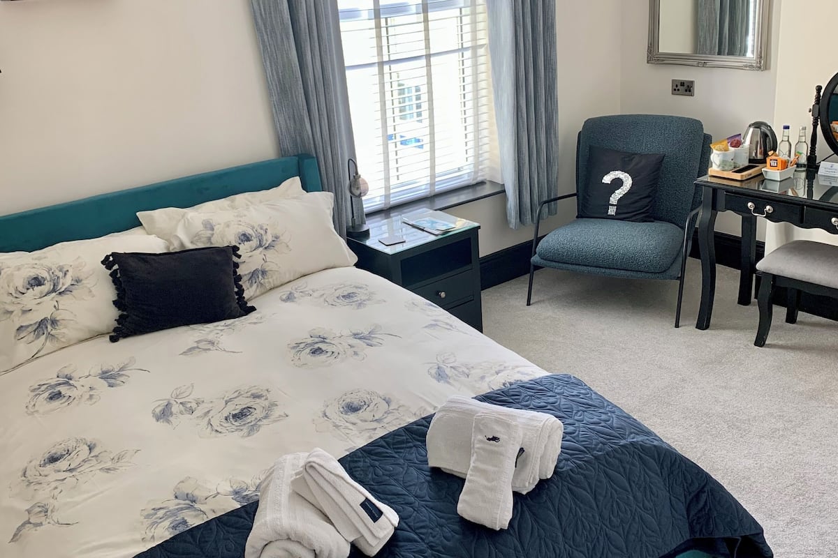 Una habitación de hotel con una cama grande, un escritorio con silla, una ventana con cortinas y un espejo en la pared.