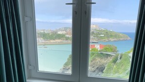 Ein Zimmer mit zwei grünen Stühlen, die zu einem Fenster mit Blick auf die Küste, Gebäude und eine Brücke zeigen.