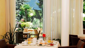 Une table de petit-déjeuner dressée avec des assiettes, des tasses et un pichet, donnant sur un jardin luxuriant et offrant une vue sur les montagnes.