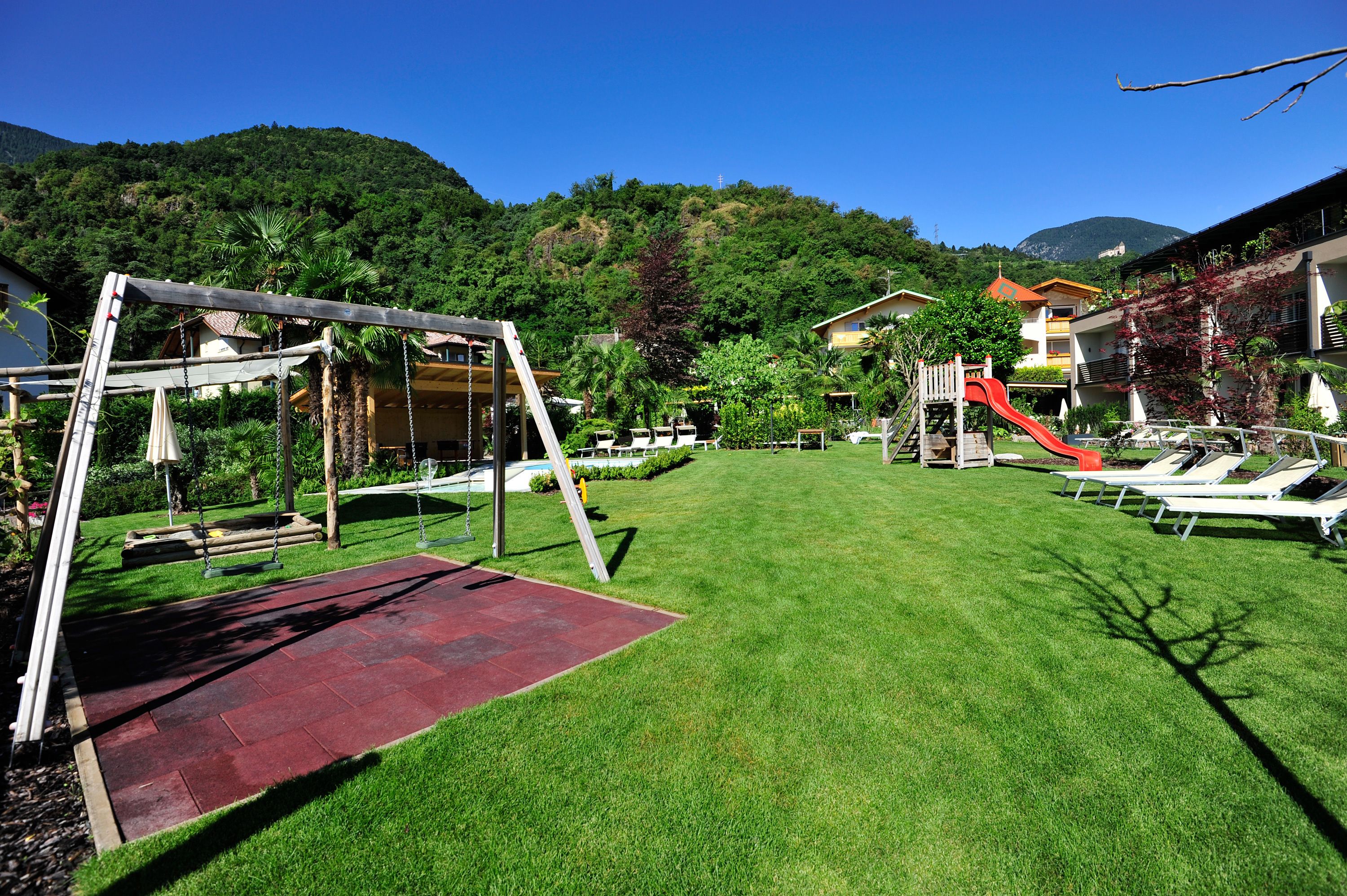 A well-maintained outdoor area with a swing set, a red slide, and lounge chairs.
