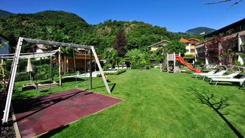 A well-maintained outdoor area with a swing set, a red slide, and lounge chairs.