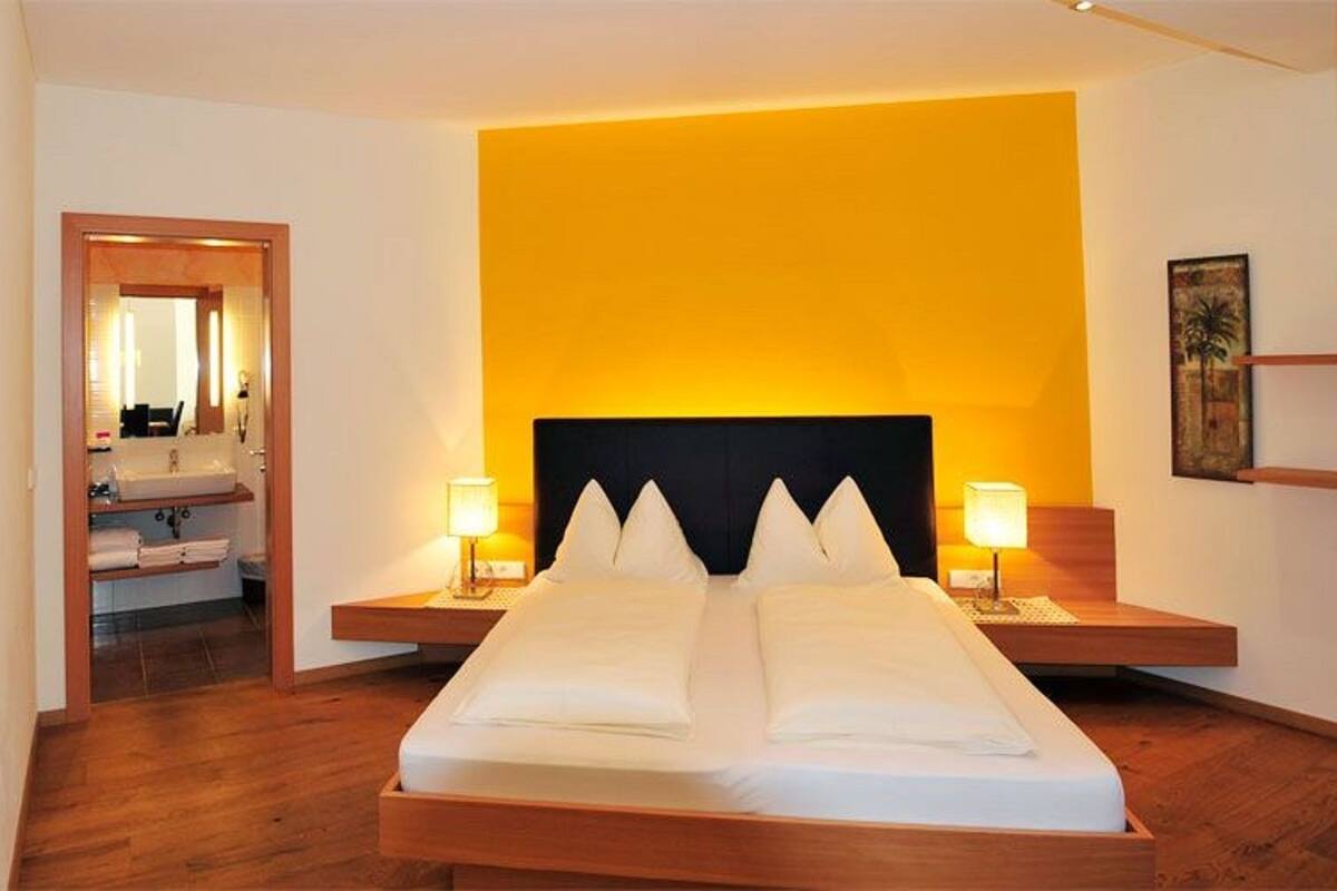 Ein Hotelzimmer mit einem großen Bett, zwei Nachttischen, einem Spiegel und einem durch eine offene Tür einsehbaren Badezimmer.