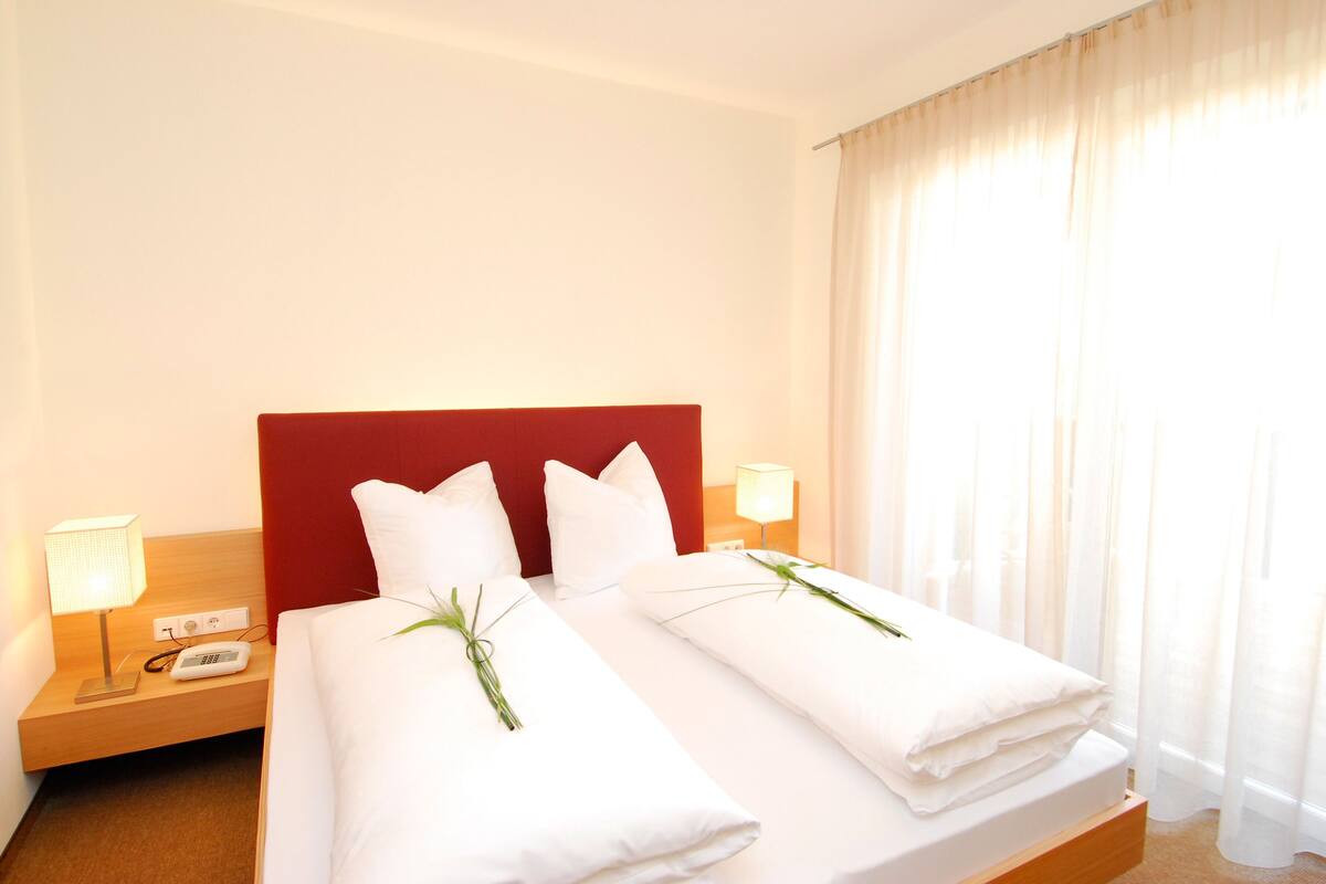 Ein Hotelzimmer mit rotem Kopfteil, zwei Betten mit weißen Laken, einem Nachttisch mit Lampe und einem Telefon.