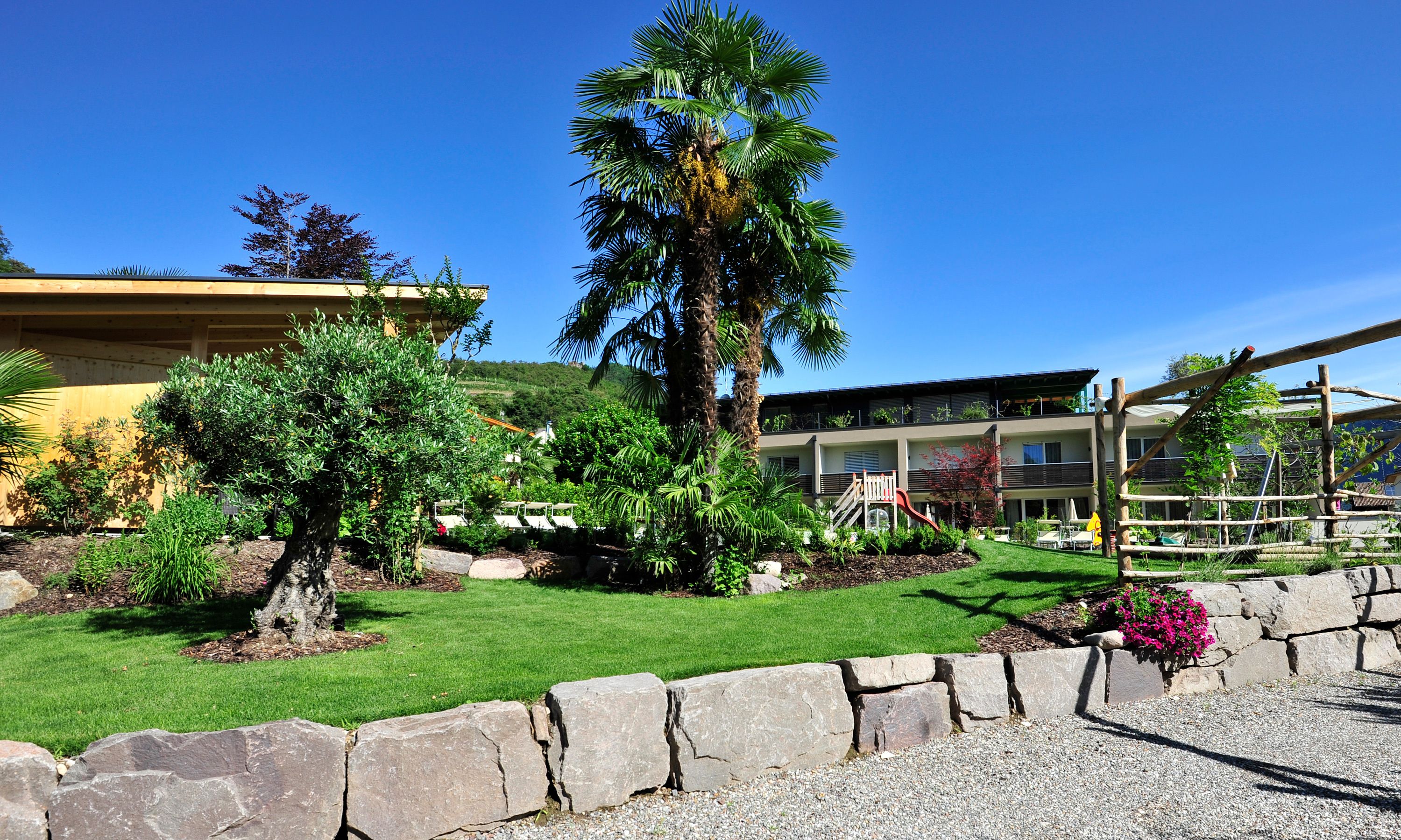 Ein Hotel mit gepflegtem Garten, einer Palme und einem Spielbereich.