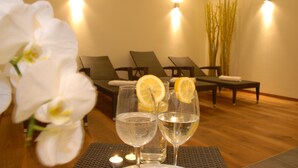 Une salle de spa avec deux verres d’eau, une bougie et une orchidée blanche.
