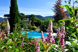 Un espace piscine offrant une vue sur les montagnes, entouré d’une végétation luxuriante et d’un grand arbre.