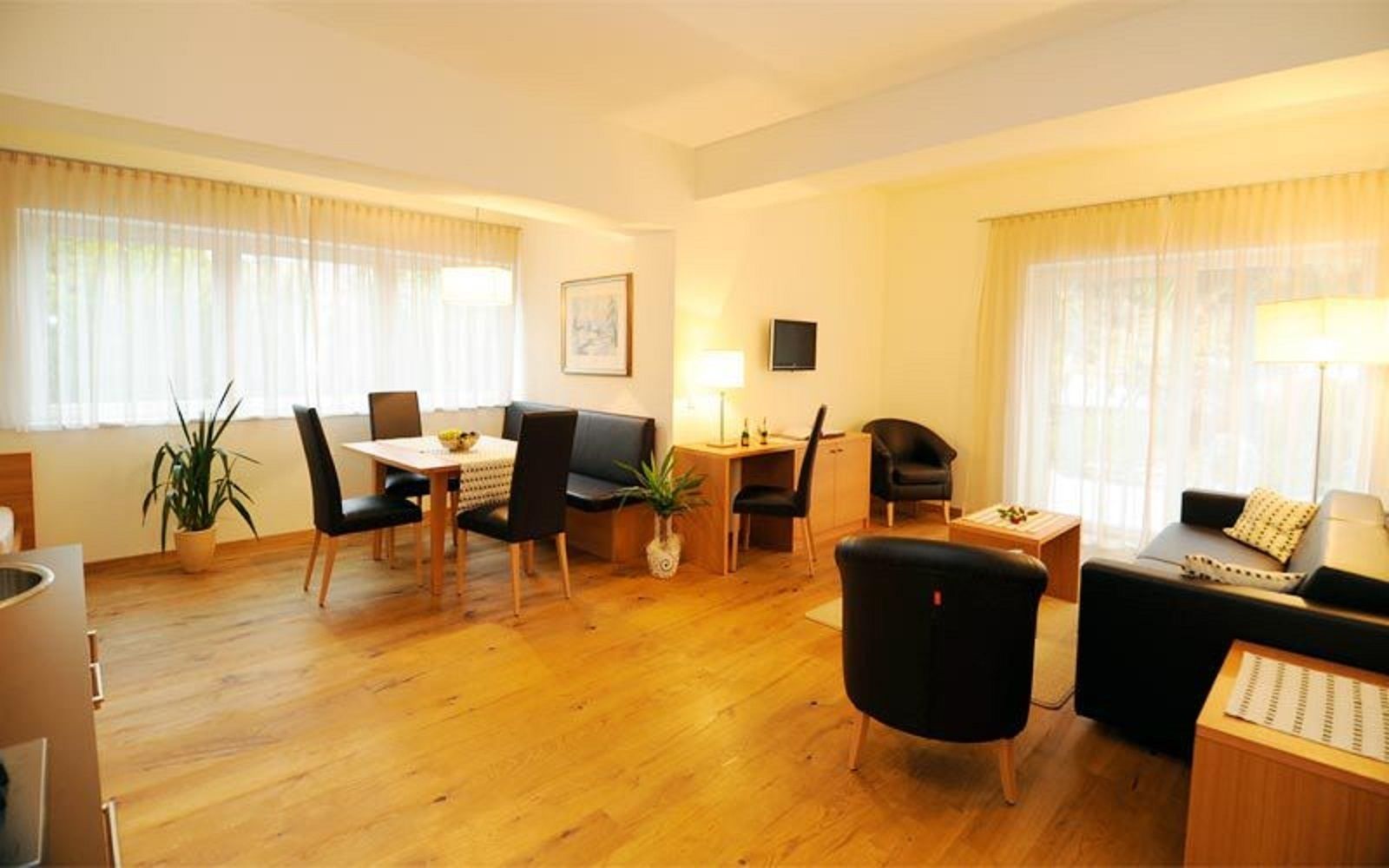 Ein großzügiger Wohnraum mit Holzboden, einem Essbereich mit Tisch und Stühlen, einer Couch und einem Fernseher an der Wand.