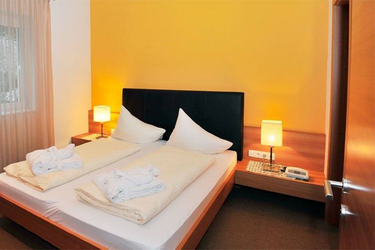 Ein Doppelbett mit weißen Bettwäsche und Handtüchern, zwei Nachttische mit Lampen und ein hölzernes Kopfteil.