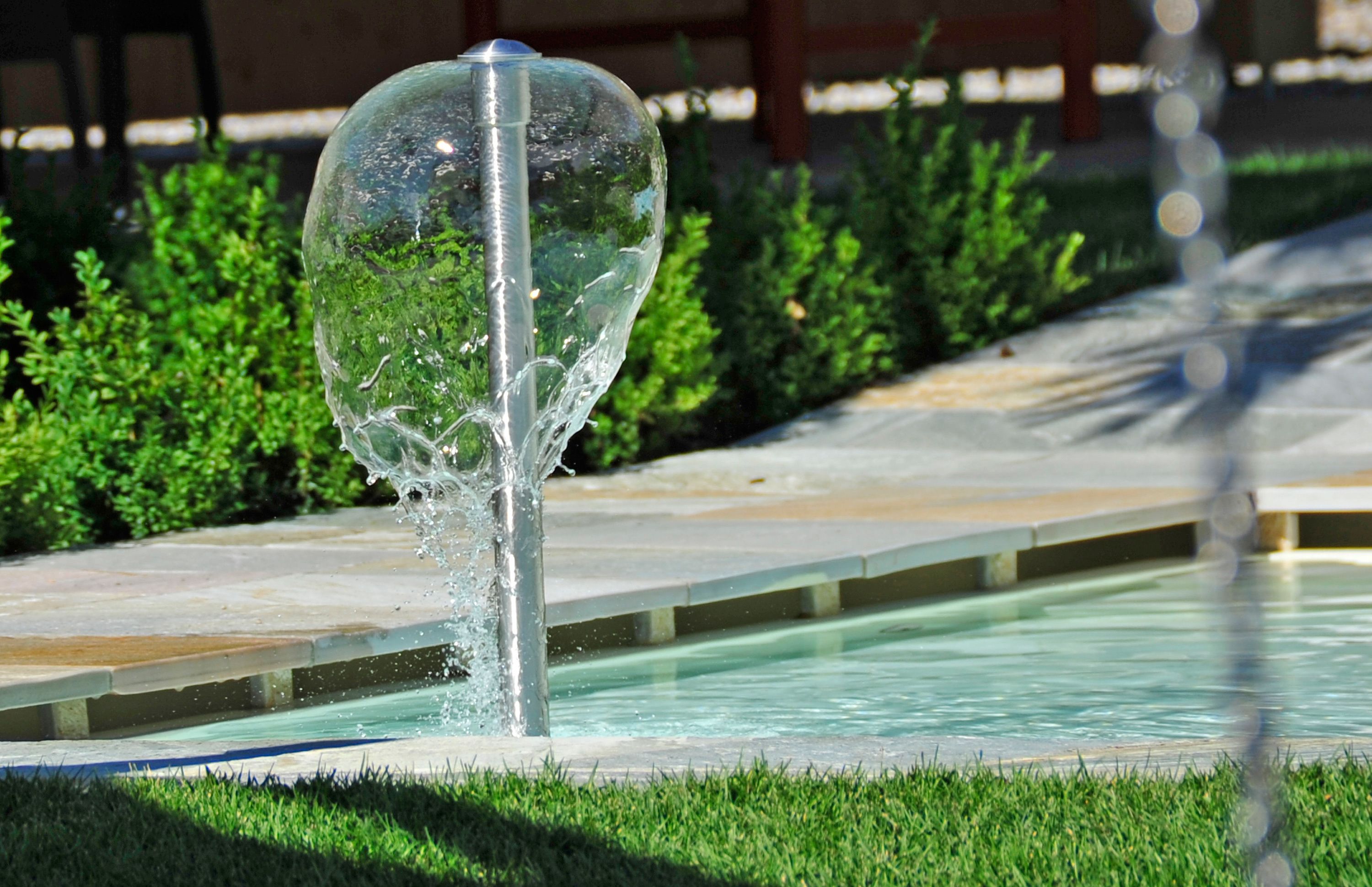 Un elemento decorativo acquatico con una struttura in vetro trasparente, inserito in un’area paesaggistica.