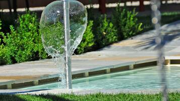 Un elemento decorativo acquatico con una struttura in vetro trasparente, inserito in un’area paesaggistica.