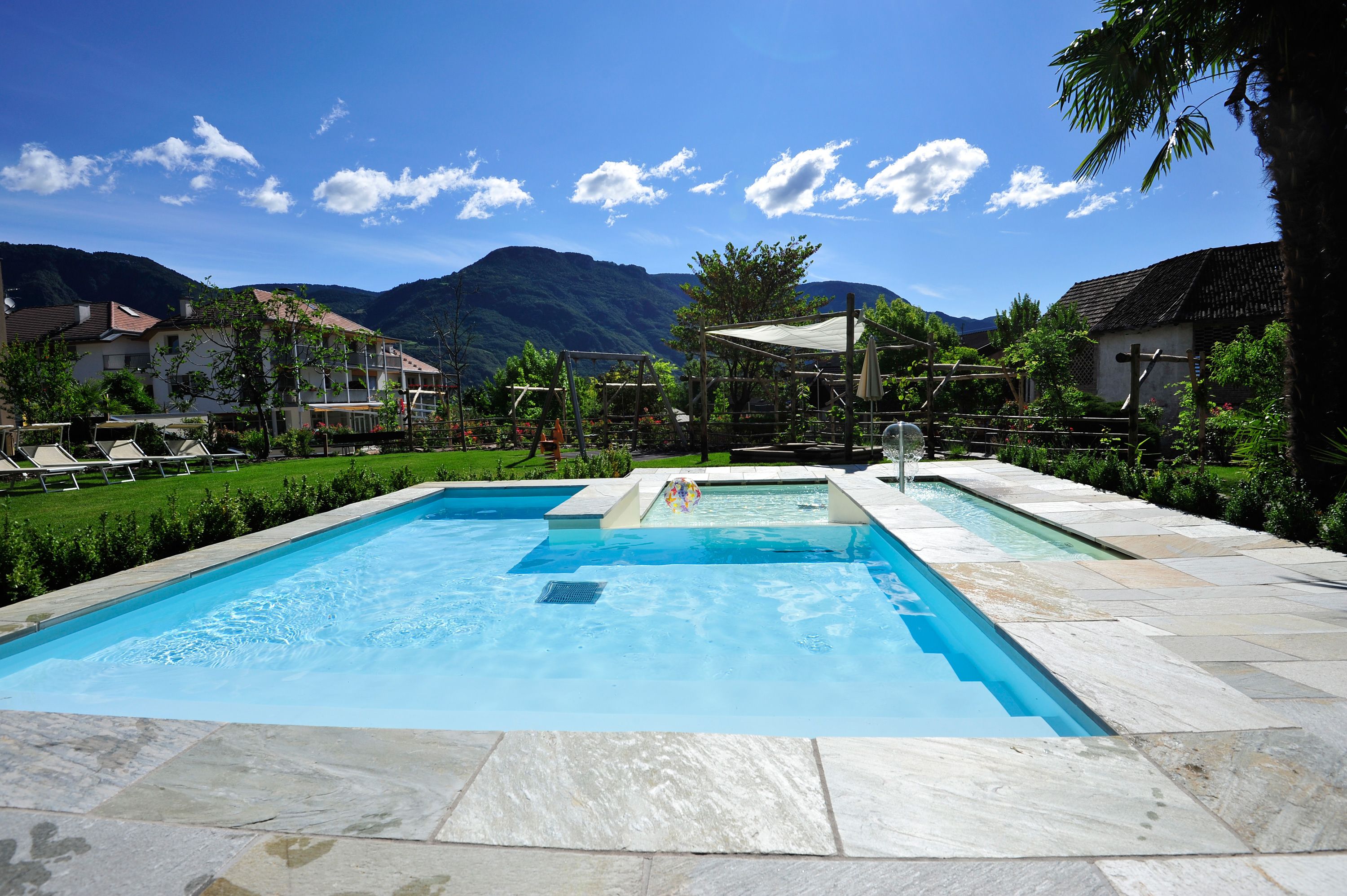 Une piscine rectangulaire bordée de pierres, entourée d’un jardin et offrant une vue sur les montagnes.