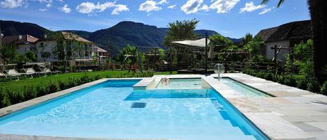 Une piscine rectangulaire bordée de pierres, entourée d’un jardin et offrant une vue sur les montagnes.