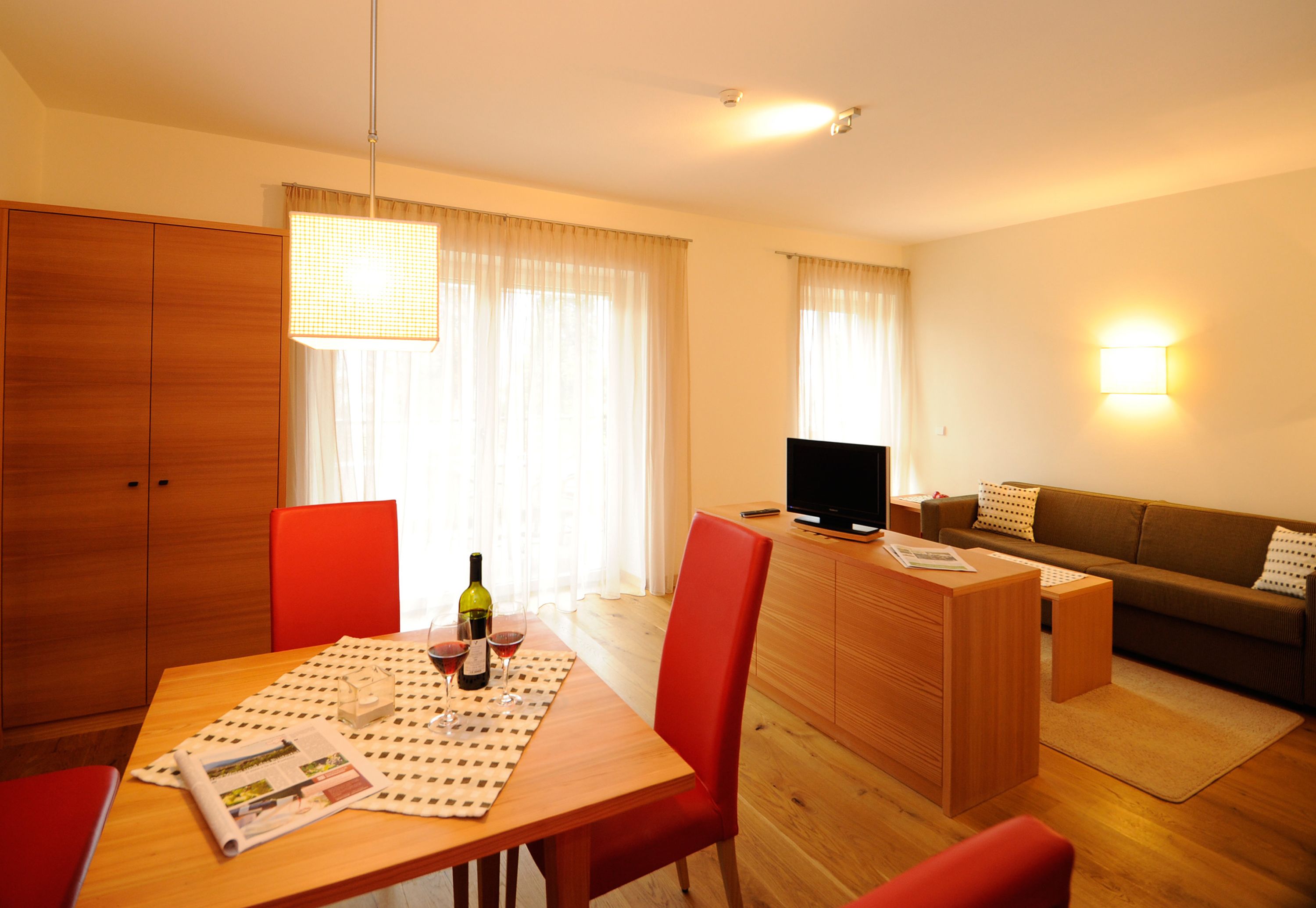 Una sala de estar moderna con una mesa de comedor de madera, sillas rojas, un sofá y un televisor.
