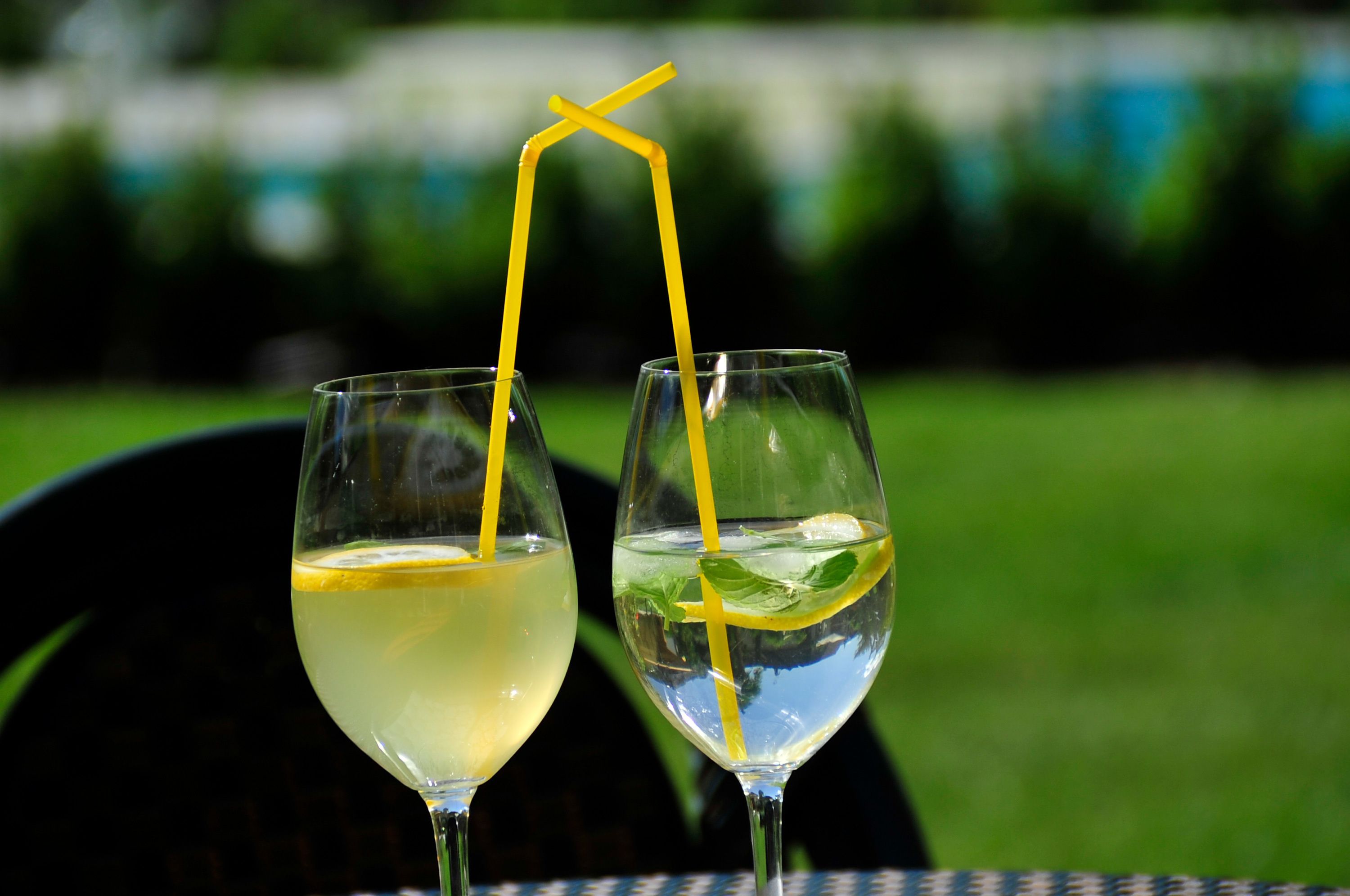 Two glasses of a light-colored beverage with yellow straws and lemon slices, placed on a table with a blurred green background.