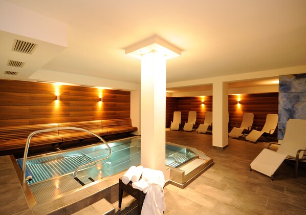 Un espace spa comprenant un bain à remous, des chaises longues et un coin salon avec des serviettes à disposition.