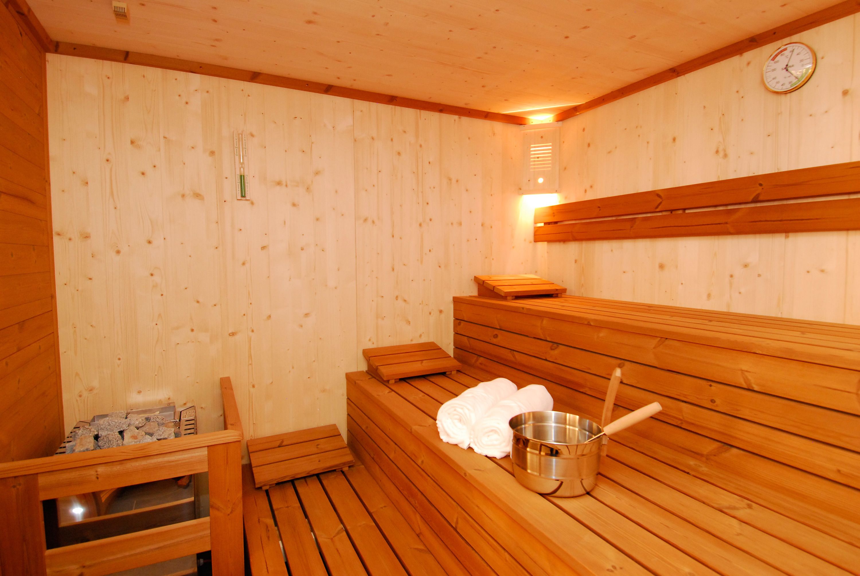 A wooden sauna with benches, a metal bucket, and towels.
