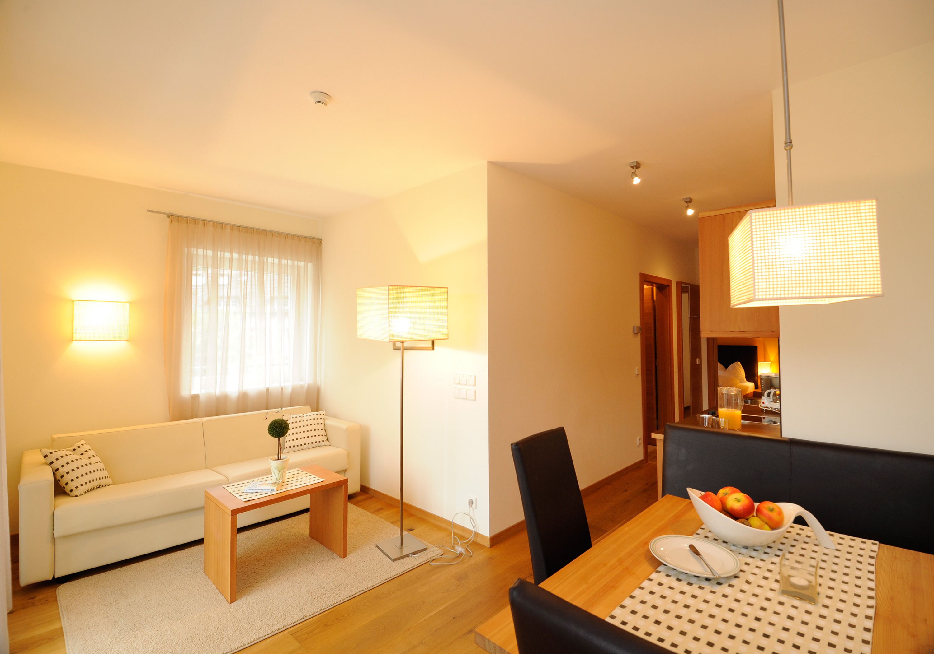Un salon moderne comprenant un canapé, une table basse, une table à manger avec des chaises, et un coin cuisine à l’arrière-plan.