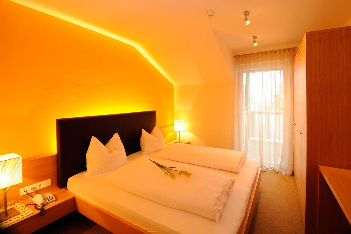 Ein Hotelzimmer mit einem großen Bett, einer Nachttischlampe, einem Telefon und einem Fenster mit Vorhängen.