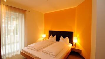 A hotel room with a large bed, two bedside lamps, and a window with sheer curtains.