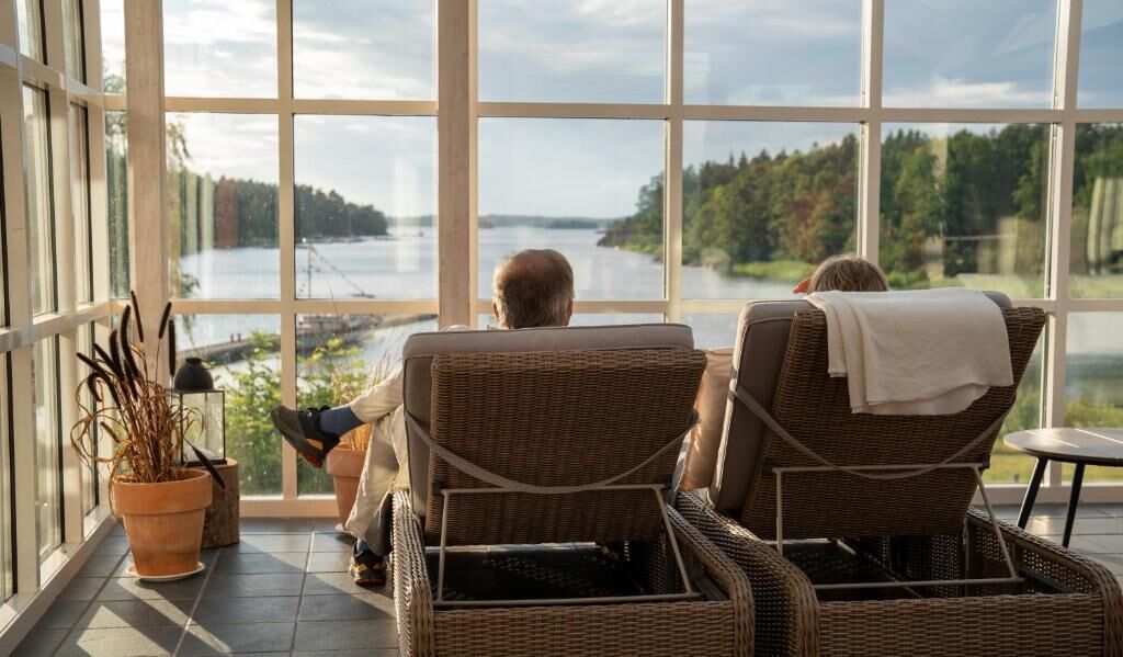Deux fauteuils en osier placés face à une grande fenêtre donnant sur un lac.