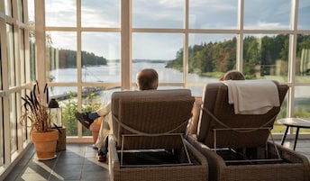 Dos sillas de mimbre mirando hacia una ventana grande con vista a un lago.