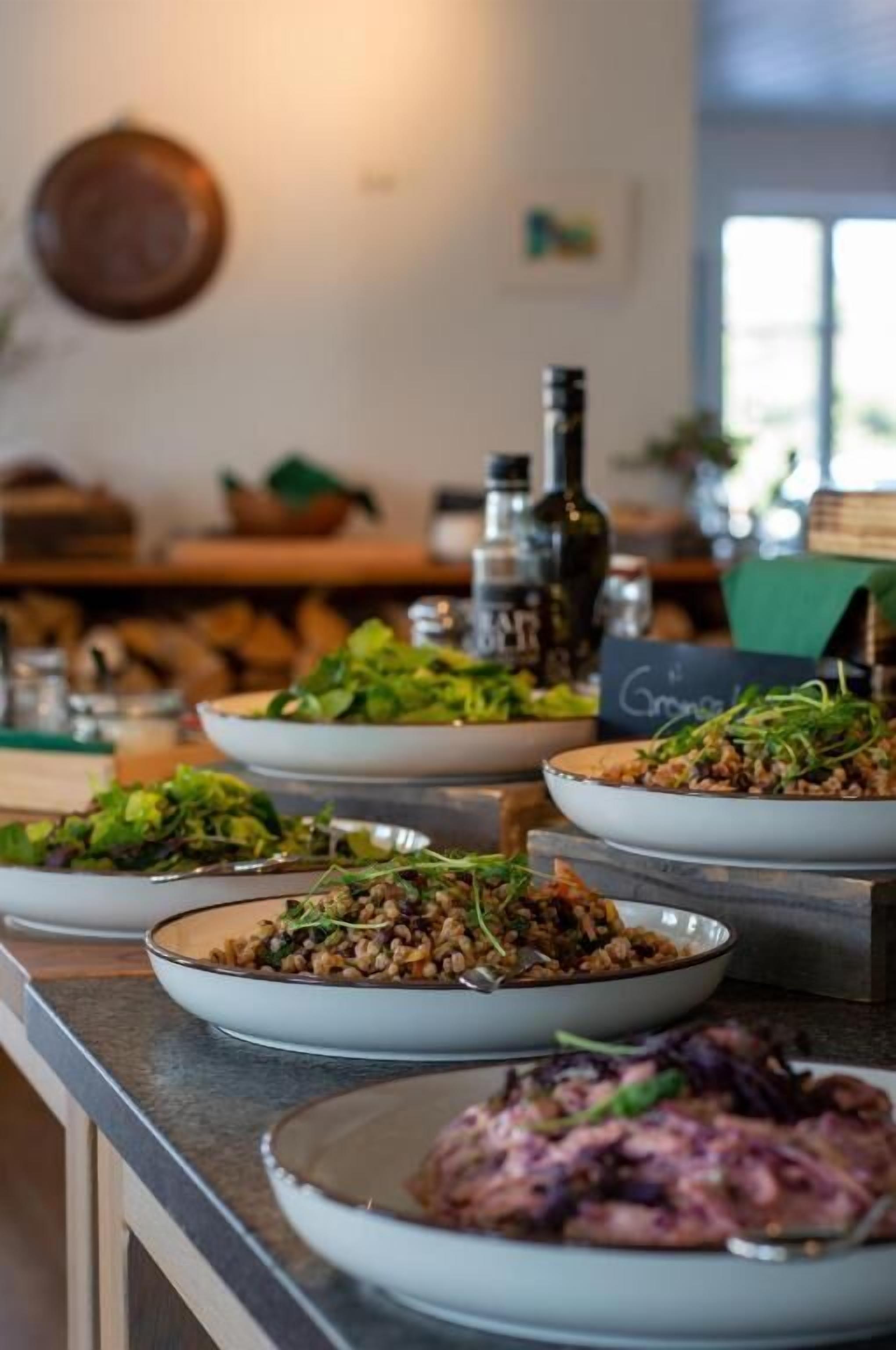 Un buffet con diversi piatti, tra cui insalate e un piatto di carne, in una sala da pranzo con un bancone e un menu scritto alla lavagna.