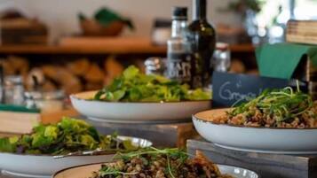 Un buffet con diversi piatti, tra cui insalate e un piatto di carne, in una sala da pranzo con un bancone e un menu scritto alla lavagna.