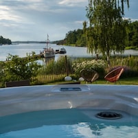 Un jacuzzi con vistas a un lago y barcos, rodeado de vegetación y mobiliario exterior.