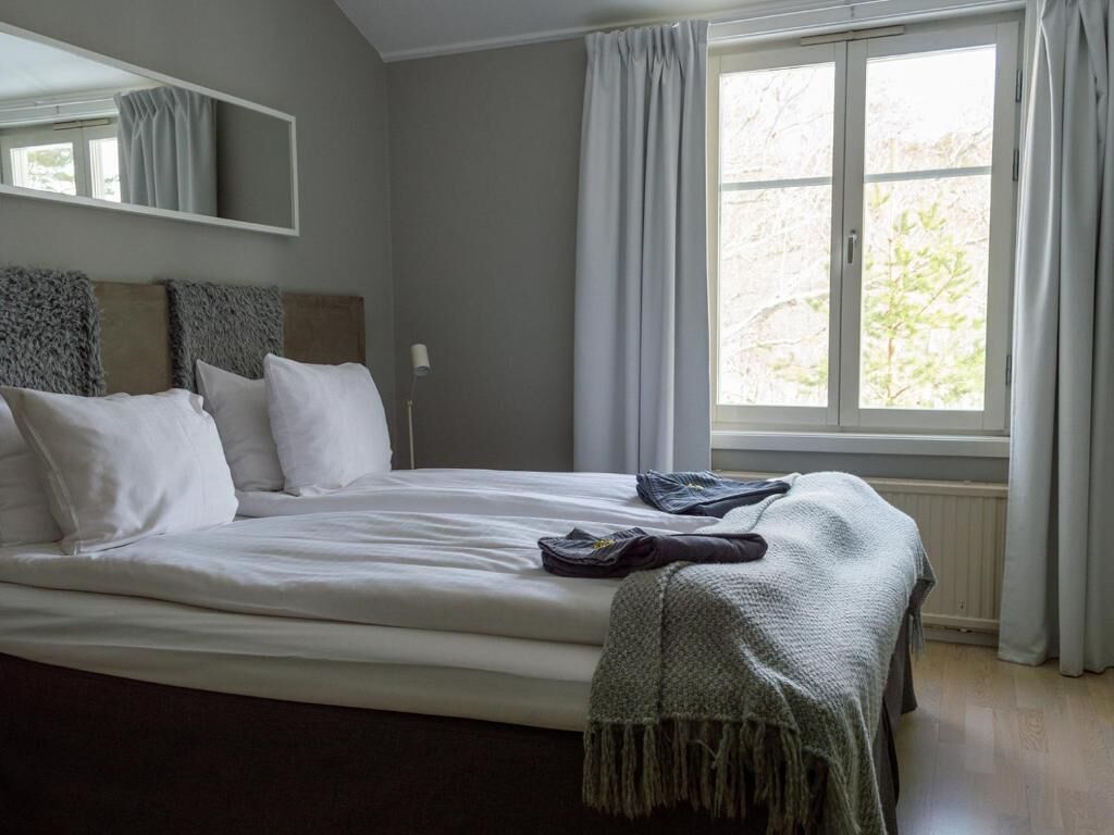A bedroom with a large bed, a window with curtains, a mirror above the bed, and a radiator below.