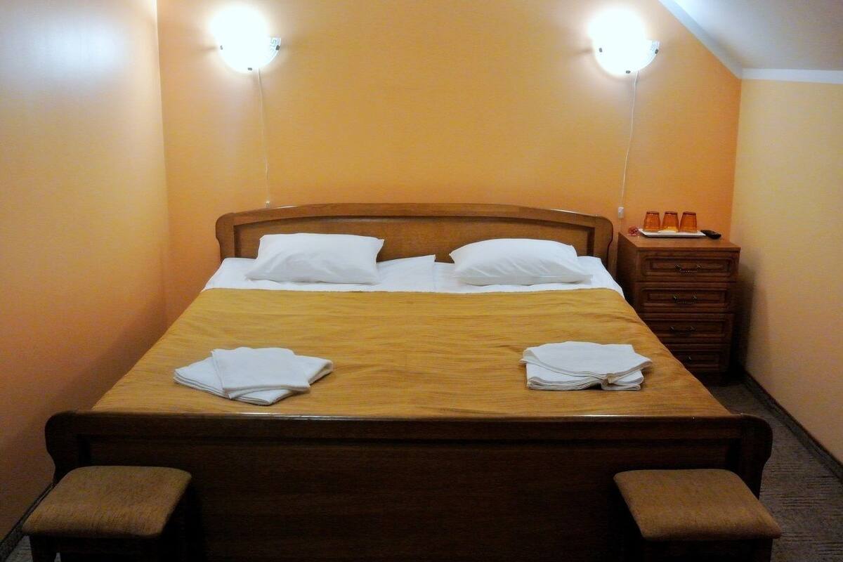 A neatly made bed with pillows and folded towels, a wooden headboard, and bedside tables with lamps.