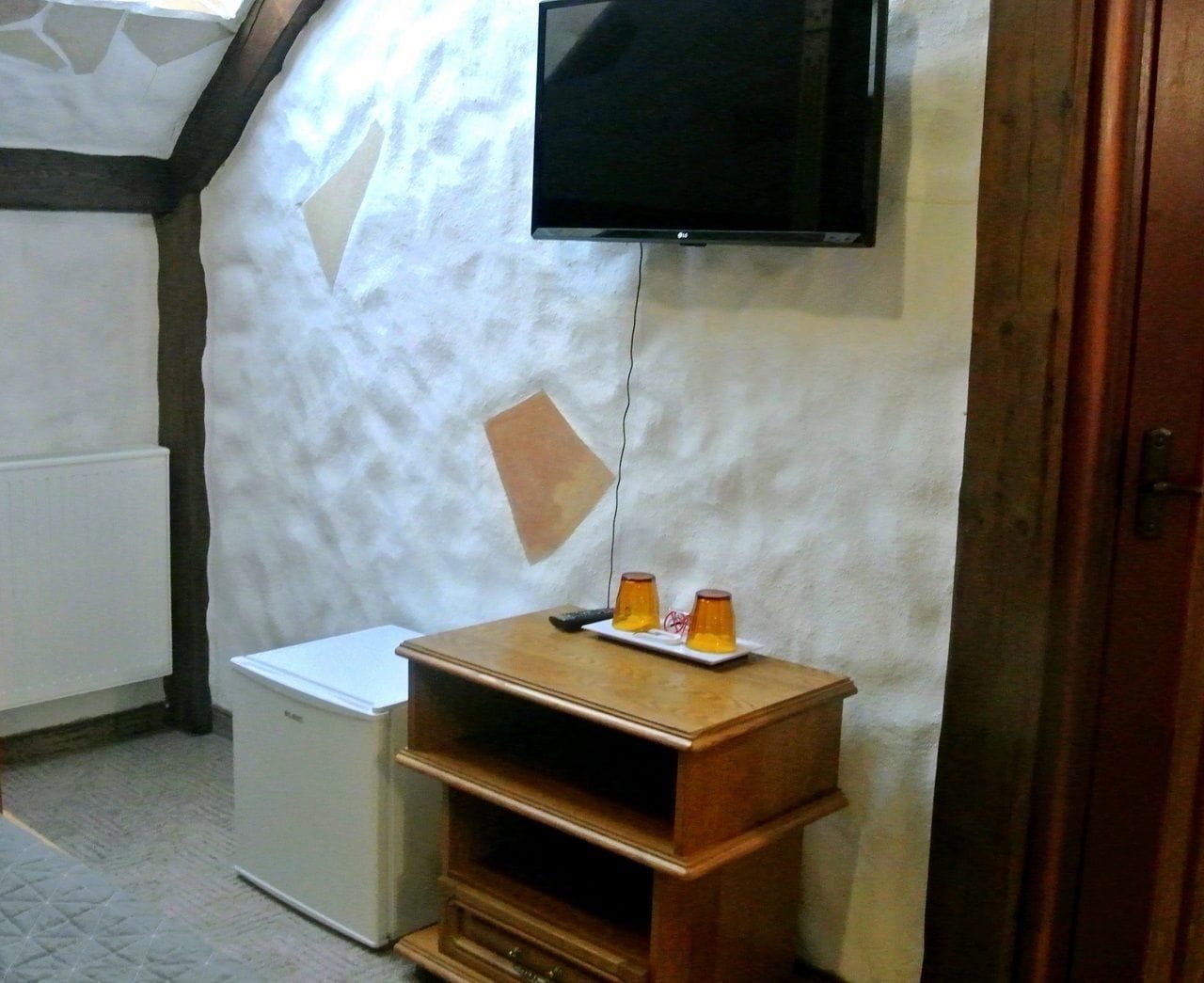 A small room with a white radiator, a wooden cabinet, and a television mounted on the wall.