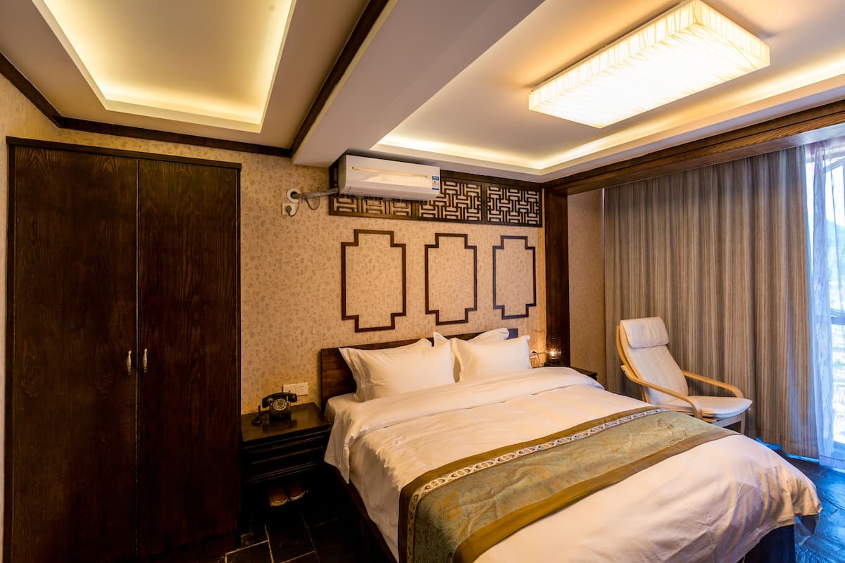 A hotel room with a large bed, a chair, a wardrobe, and a ceiling light.
