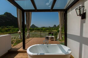 A balcony with a glass enclosure, a bathtub, and a table with chairs. - Moon Flower Hotel (Guilin)