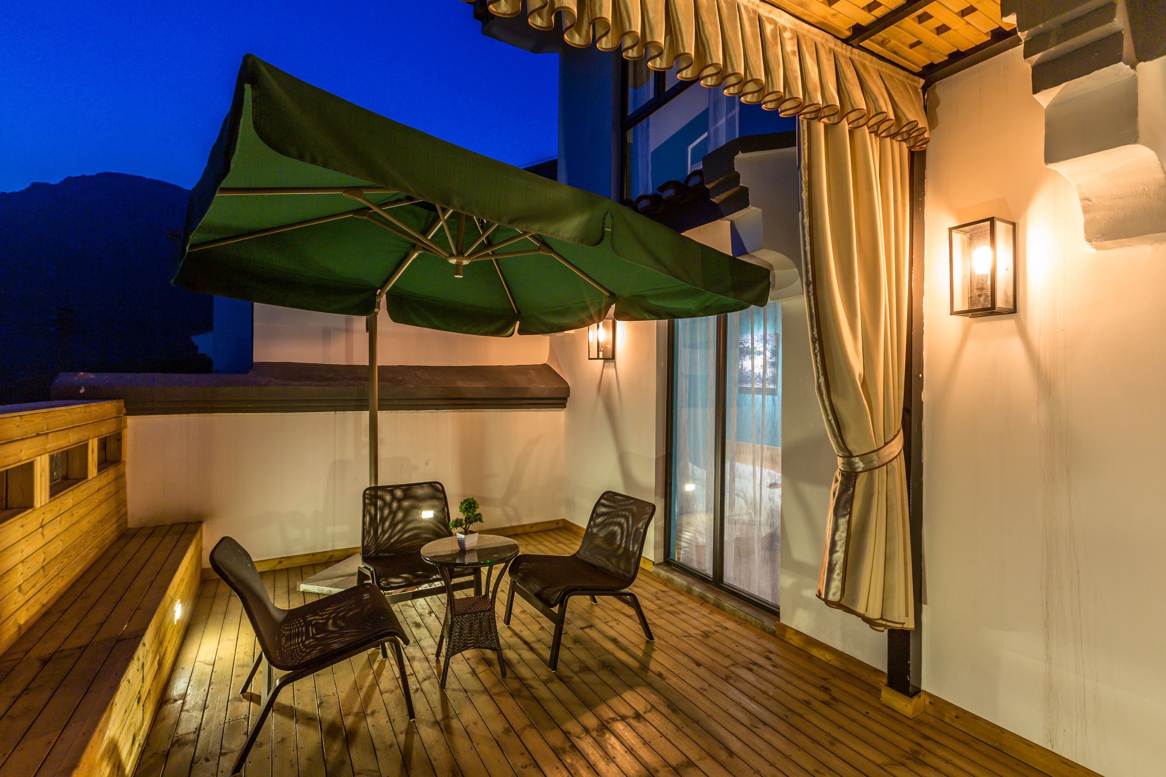 A wooden deck with a table and chairs, a green umbrella, and a wooden bench.