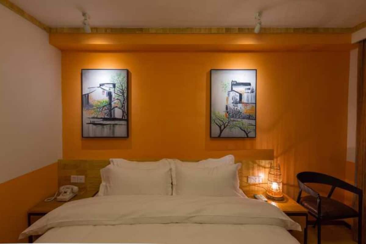 A hotel room with a bed, a nightstand, a chair, and two paintings on the wall.